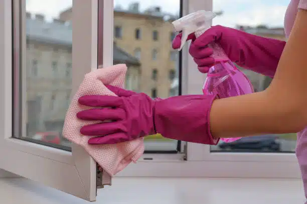 Young woman cleaning window frame with rag and detergent at home, closeup